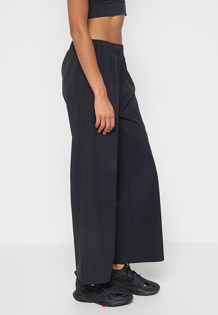 Pantalons larges noirs en tissu lisse et léger. Dotés d'une taille élastique et de coutures verticales pour un détail supplémentaire.