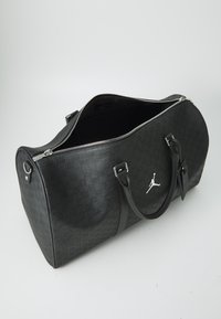 Borsa duffle nera con motivo in rilievo, zip argentate e logo Jumpman. Texture liscia e doppie maniglie per il trasporto.