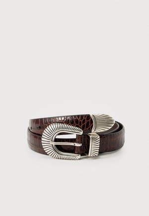 Ceinture en cuir de crocodile brun foncé avec boucle décorative en métal argenté texturé et embout, enroulée sur un fond blanc.