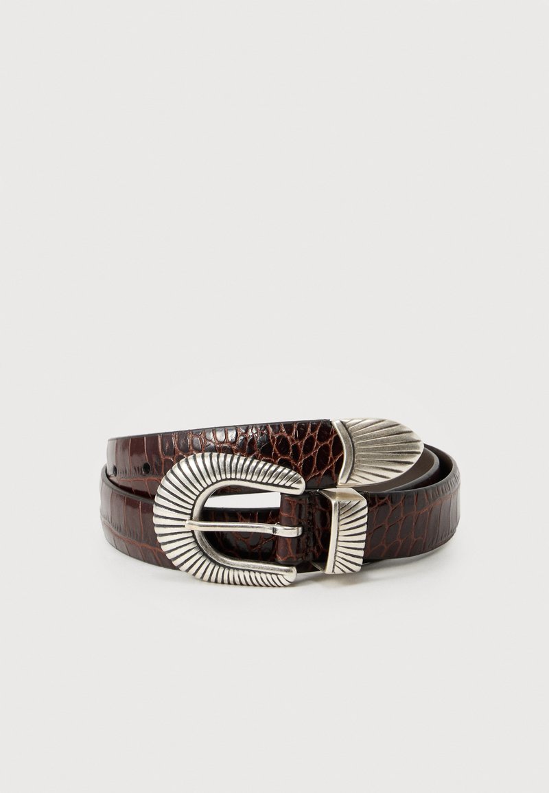 Ceinture en cuir de crocodile brun foncé avec boucle décorative en métal argenté texturé et embout, enroulée sur un fond blanc.