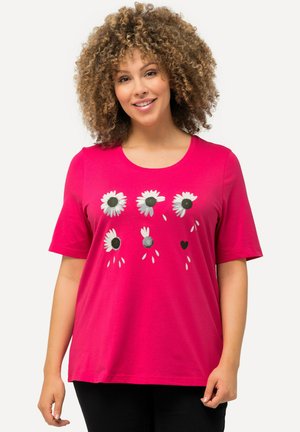 T-shirt di cotone rosa con maniche corte, caratterizzato da una grafica floreale di margherite con centri neri e un piccolo design a forma di cuore.