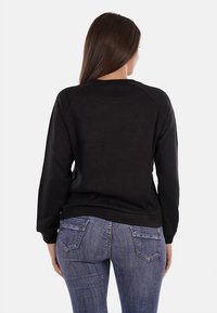 Felpa nera con maniche a raglan, morbido tessuto e scollo rotondo. Abbinata a jeans blu con tasche posteriori.