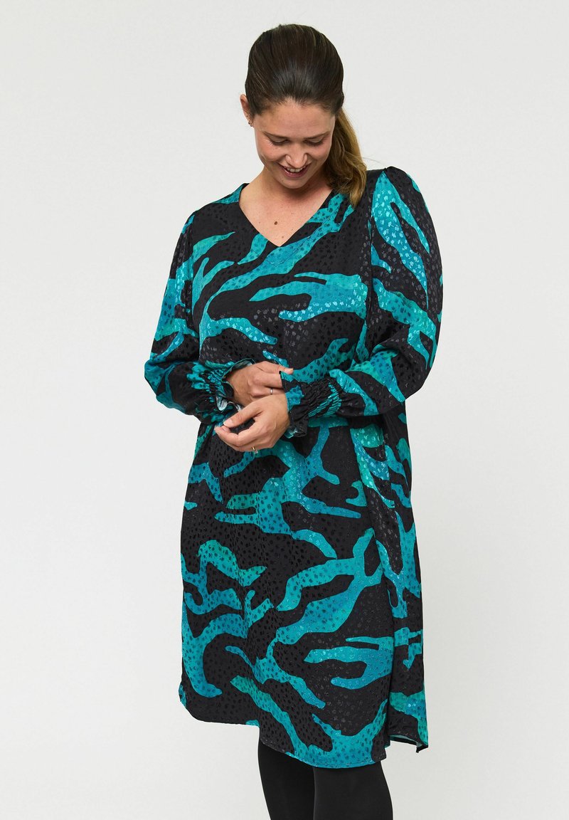 Langharig jurk met een zwarte basis en teal abstracte patronen, een V-halslijn en geplooide mouwen. Gemaakt van lichtgewicht stof.