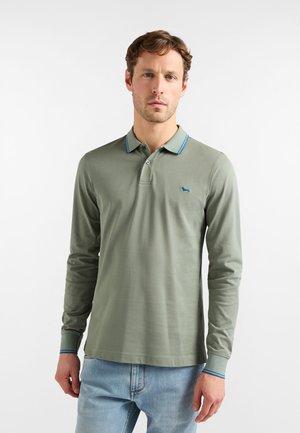 Polo a maniche lunghe in cotone verde oliva, con colletto a righe blu e piccolo logo ricamato sul petto. Indossato con jeans.