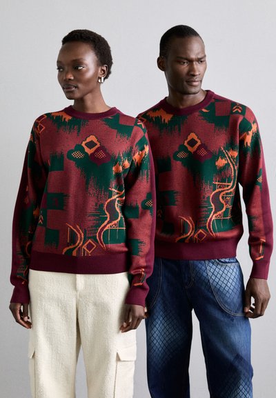 Maroon knit sweaters with geometric and abstract patterns in green and orange, featuring ribbed cuffs and hem, worn by two models.