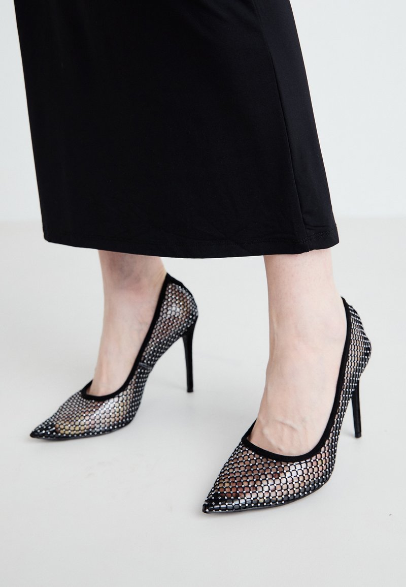 Schwarze Netz-High Heels mit spitzem Zehenbereich und dünnem Stiletto-Absatz. Das gemusterte Design verfügt über kreisförmige Aussparungen, die einen halbtransparenten Look bieten.