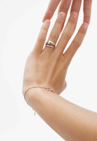 Pulsera de estrellas de plata en la muñeca con una fina cadena. Textura suave, diseño minimalista. Anillo de plata adicional en el dedo adyacente.