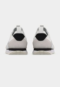 Ζευγάρι λευκών και γκρι αθλητικών παπουτσιών με μαύρες λεπτομέρειες στη φτέρνα και λευκές θηλιές, εμφανιζόμενα από πίσω σε απλό λευκό φόντο.