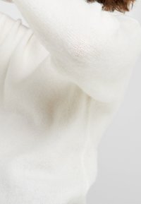 Witte, fluffy trui van zacht materiaal, met een gestructureerd breipatroon en een relaxte pasvorm. Het kledingstuk heeft lange mouwen en een ronde halslijn.