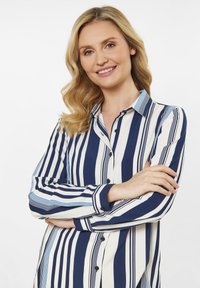 Blusa a righe blu navy e bianca con chiusura a bottoni, dotata di righe orizzontali e verticali, colletto e maniche lunghe. Tessuto morbido.