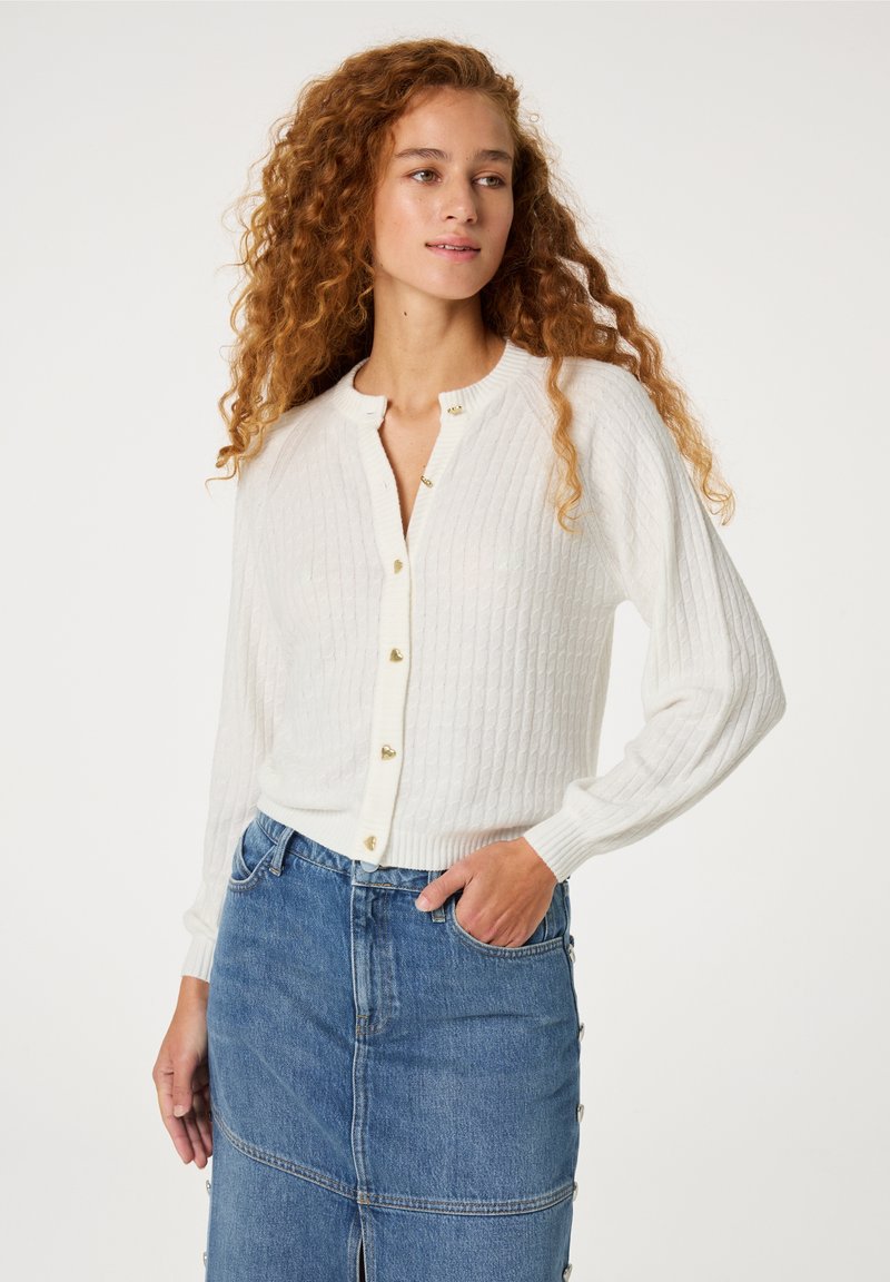 Witte geribbelde cardigan met een ronde hals, voorzien van goudkleurige knopen, gedragen over een denimrok met zijknopen.
