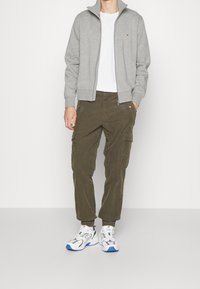 Gray zip-up sweatshirt, white t-shirt, olive cargo pants, and white sneakers with blue accents, featuring a relaxed fit and structured design.