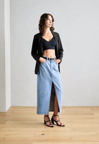 Fekete blazer fekete cropped toppal, világoskék farmer szoknyával, amelynek elülső része hasítékkal rendelkezik. A megjelenést fekete magassarkú szandálok egészítik ki.