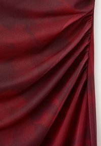 Tissu rouge profond avec des plis froncés d’un côté créant des plis diagonaux, montrant la texture et des variations subtiles de couleur.