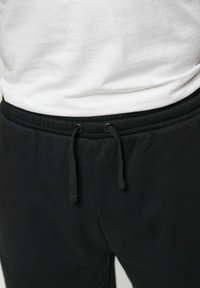 Fekete melegítő nadrág derékrésze, középen megkötött, látható húzózsinórral, fehér begombolt inggel párosítva.