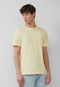 Żółta bawełniana koszulka z okrągłym dekoltem i krótkimi rękawami. Posiada subtelne logo na piersi. W zestawie z jasnoniebieskimi dżinsami.