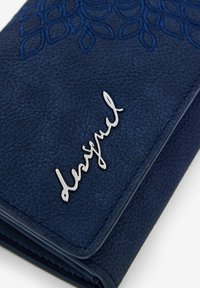 Dunkelblaues Portemonnaie aus strukturiertem Material mit einem geprägten Blattmuster und einem silbernen metallischen Logo. Kompaktes Design mit gefalteten Kanten.