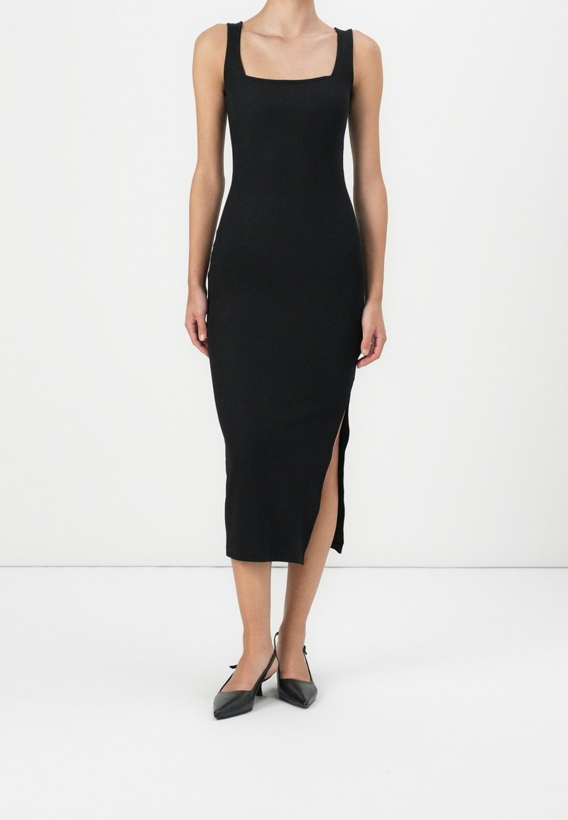 Czarna, dopasowana, bezrękawnikowa sukienka z kwadratowym dekoltem i rozcięciem po bokach. Modelka połączyła ją z czarnymi szpilkami o ostrym nosku. Gładka tekstura.