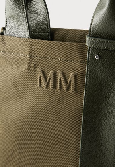 Κοντινό πλάνο τσάντας tote από καμβά ελιάς με λαβές από υφαστό δέρμα και το ανάγλυφο "MM" στο ύφασμα.