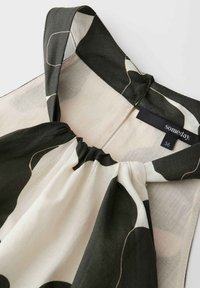 Gros plan sur l'encolure d'une robe à motif noir et blanc avec tissu froncé et larges bretelles, étiquette taille 36 visible.