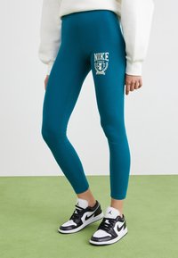 Turkosa leggings med en åtsittande design, med en vit Nike-logotyp och emblem på låret, kombinerat med svartvita sneakers.