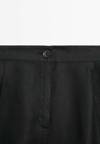 Un pantalon en lin noir avec une fermeture à bouton à l'avant, deux poches latérales et une texture lisse au design classique.