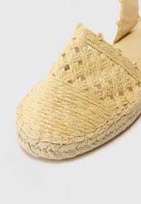 Espadrille jaune clair avec tige en paille tissée, bout arrondi et semelle en jute cousue. Présente un motif en croisillon et une doublure intérieure lisse.