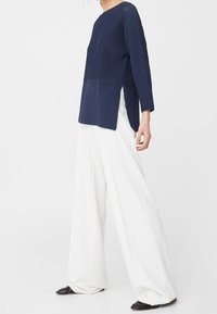 Top en maille côtelée marine avec un ourlet asymétrique, associé à un pantalon blanc à jambes larges et des ballerines noires. Présente des manches longues et une coupe décontractée.