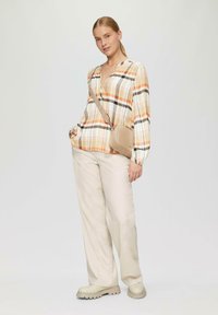 Karierte Bluse in Orange, Gelb und Schwarz; leichtes Material, lange Ärmel. Beige Hosen und passende Umhängetasche. Chunky beige Schuhe.