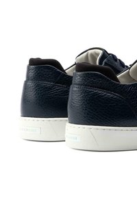 Navy leather sneakers with textured finish, white rubber sole, and a low-cut design. Notable black accents on the collar and lace area.