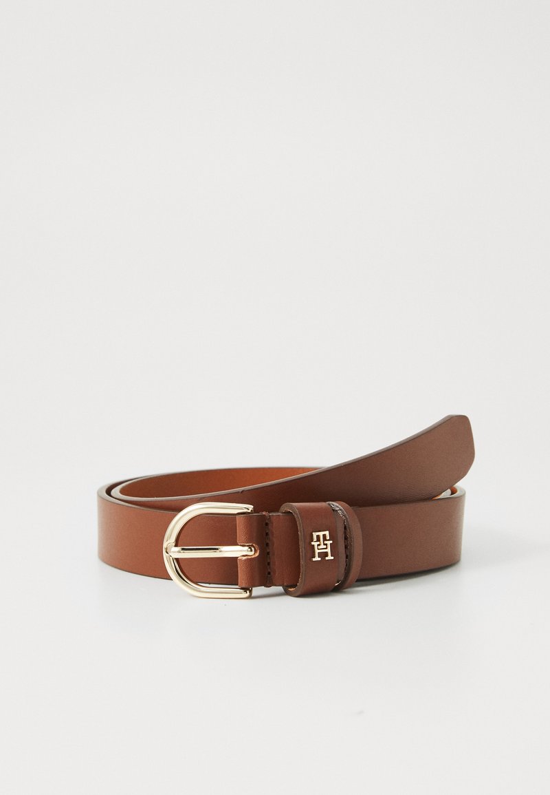 Brauner Leder Gürtel, aufgerollt mit goldener Metall Schnalle und "TH" Logo Detail an der Gürtelschlaufe vor einem weißen Hintergrund.