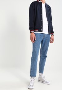 Marine bombersjas met witte en rode gestreepte manchetten, gecombineerd met een witte poloshirt, blauwe jeans en witte high-top sneakers.