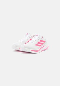 Baskets de sport blanches avec des accents roses, présentant un dessus texturé, un design à trois bandes et une semelle rembourrée pour le soutien.