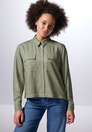 Lys grøn, langærmet skjorte med knaplukning, to brystlommer, krave og en glat tekstur, parret med blå denimjeans.