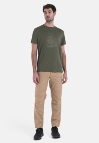 Olivgrön t-shirt med en vit bergsgraphic, matchad med tan cargo-byxor och svarta träningsskor. Slätt tyg med en avslappnad passform.