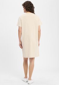 Kurzes beiges Kleid aus weichem Stoff mit kurzen Ärmeln, einem runden Ausschnitt und einem geraden Schnitt, das gerade über die Knie fällt.