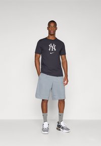 Dark gray athletic t-shirt with a light gray NY logo, paired with light gray shorts, gray socks, and black and white sneakers.