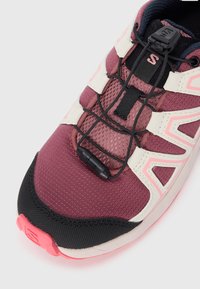 Baskets de sport bordeaux et blanches avec tige en mesh, système de laçage dynamique, accents noirs et semelle texturée. Présente un détail réfléchissant.
