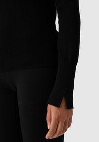 Černý pletený svetr s dlouhými rukávy a rozparky, vyrobený z měkkého materiálu. Střih je slim, s žebrovaným lemem a manžetami.