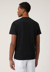 Zwarte T-shirt met korte mouwen en ronde hals, gladde textuur, ontspannen pasvorm en rechte zoom, weergegeven vanuit de achterkant zonder zichtbare ontwerpelementen.