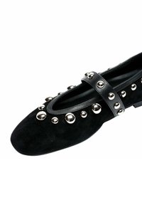 Scarpa in suede nero con borchie rotonde argento e cinturino nero sul collo del piede. Suola piatta, punta appuntita e finitura interna liscia.