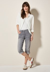 Camisa blanca de botón, pantalones cortos grises y zapatillas blancas con acentos rojos. Se puede ver la tela suave, los puños enrollados y los bolsillos delanteros.
