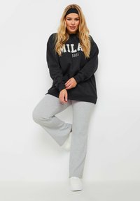 Svart oversized sweatshirt med texten "MILAN 1991", parat med ljusgrå vida sweatpants och vita sneakers. Slen textur, avslappnad design.