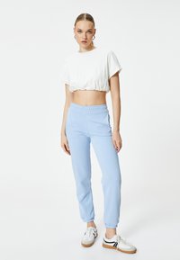 Witte cropped T-shirt met gathered zoom en korte mouwen, gecombineerd met lichtblauwe joggingsbroek met een elastische tailleband en manchetten bij de enkels.