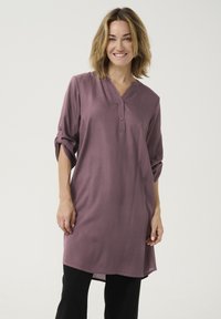 Tunika w kolorze mauve z dekoltem w serek, z rękawami o długości trzy czwarte z guzikami, o prostym kroju opadającym poniżej bioder.