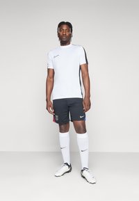 Nike sportkläder: vit kortärmad topp med svarta detaljer, svarta shorts med färgglada sidopaneler, vita strumpor och svarta fotbollsskor.