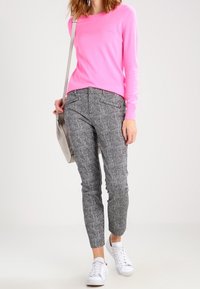 Pink long-sleeve sweater, gray textured tapered pants, and white sneakers. Model carries a gray bag, posing against a plain background.