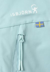 Lyseblåt stof med en glat tekstur, der har en lynlås og snoretræk. Inkluderer hvidt "ISBJÖRN" logo og et lille svensk flag-patch.