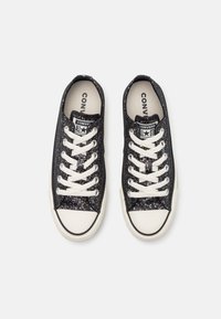 Zapatillas de lona negras con textura brillante, cordones blancos, clásica puntera de goma y logo de All Star. Forro interior suave.