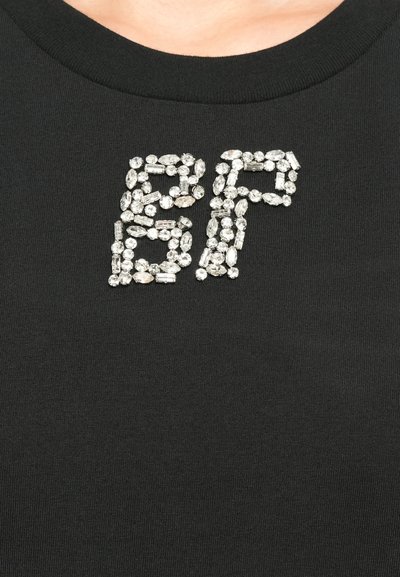 Μαύρο ύφασμα με τον αριθμό "87" στο στήθος, φτιαγμένο από μικρούς, διάφανους, περιστραμμένους κρυστάλλους που είναι τακτοποιημένοι σε δύο μεγάλους αριθμούς.